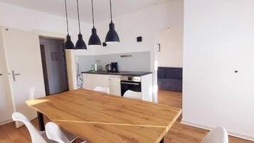 A modern kitchen with a wooden dining table, white chairs, and pendant lighting.