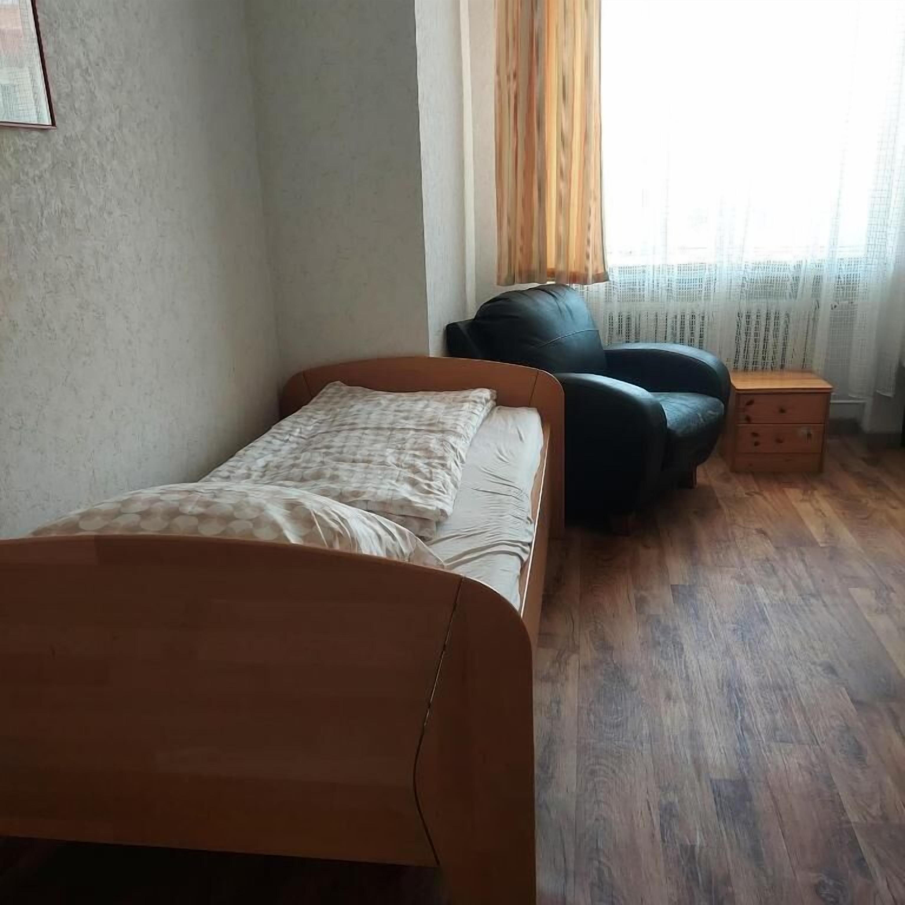 A bedroom with a bed, a chair, a nightstand, and a window with curtains.
