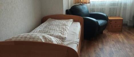 A bedroom with a bed, a chair, a nightstand, and a window with curtains.