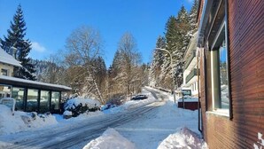 A residential street with snow-covered ground, houses, and trees.