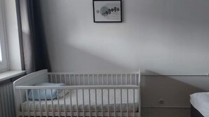 A room with a white crib, a bed, and a window with curtains.