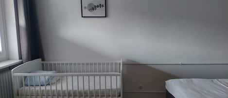 A room with a white crib, a bed, and a window with curtains.