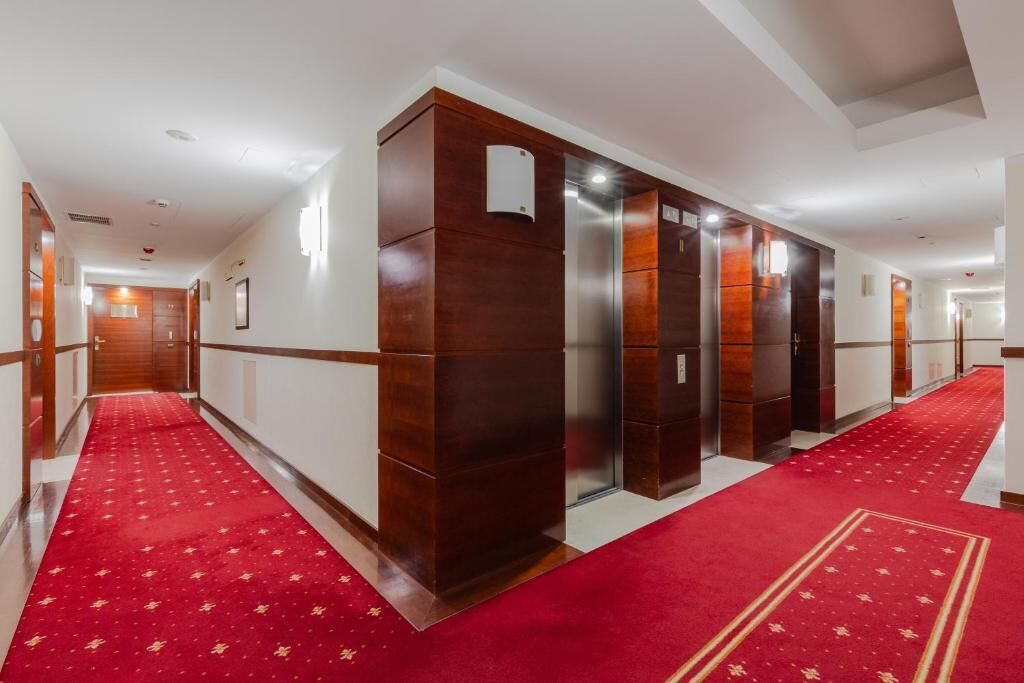 Ein Hotelgang mit rotem Teppich, Holzvertäfelung und mehreren Aufzügen.