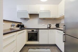 A modern kitchen with white cabinets, stainless steel appliances, and a black oven. - Bagno 2, City Center (Warszawa)
