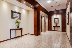 A hotel lobby with a marble floor, wooden paneling, two elevators, and a reception desk with a potted plant. - Bagno 2, City Center (Warszawa)