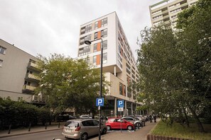 En parkeringskælder i flere etager med et blåt parkeringsskilt, omgivet af træer og parkerede biler.