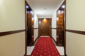 En hotelgang med rødt tæppe, trædøre og hvidt loft.