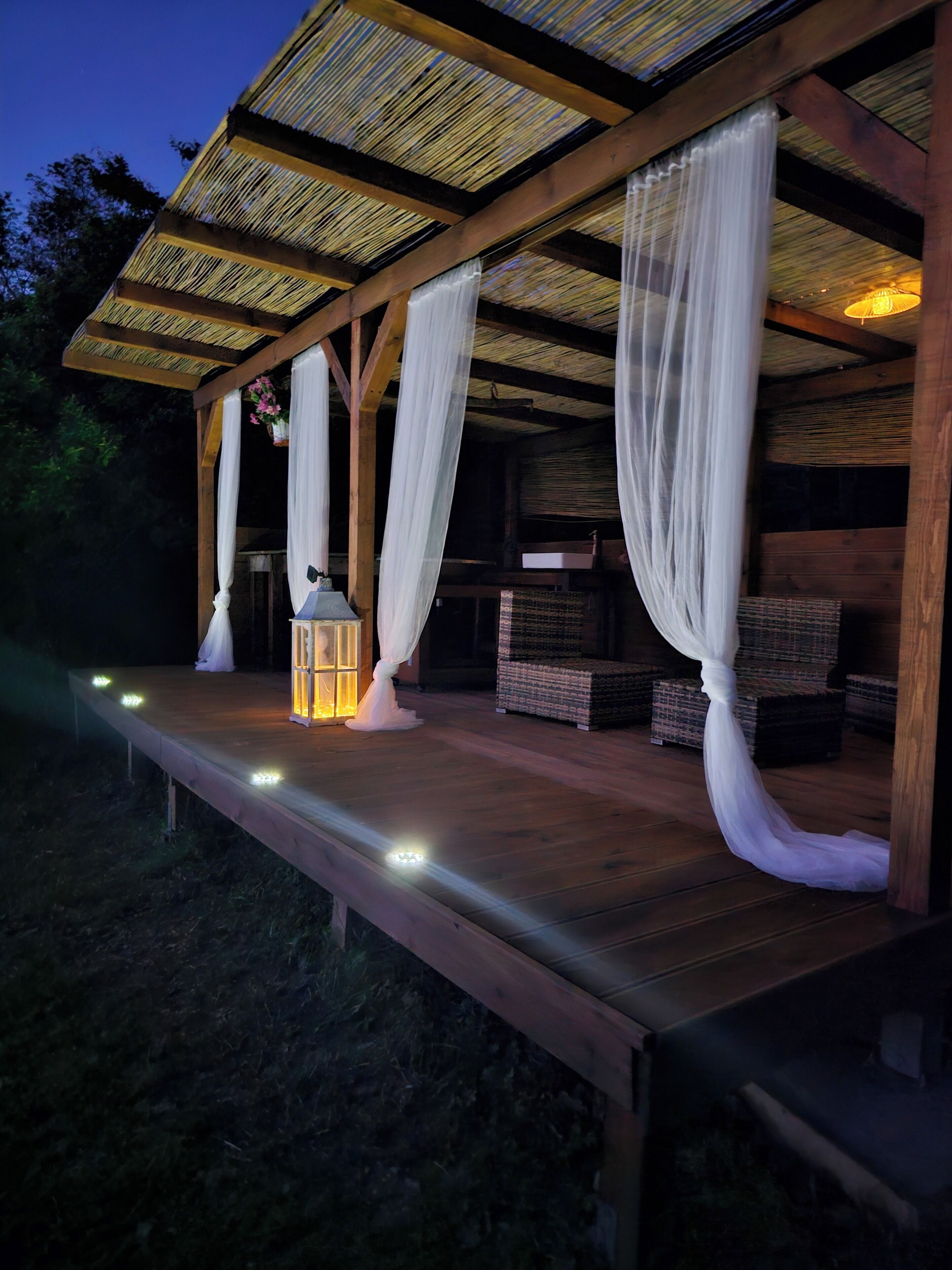 An outdoor wooden structure with a covered seating area, a hanging lantern, and a small table.