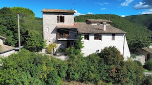 A stone building with a bell tower, surrounded by greenery and hills. - La Locanda del Tempo: an authentic stay combining charm, relaxation, and the real Italy. (Crocemarroggia)