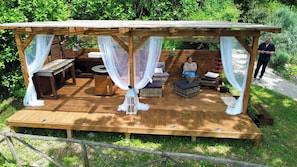 A wooden deck with a canopy, wicker furniture, and a person seated. - La Locanda del Tempo: an authentic stay combining charm, relaxation, and the real Italy. (Crocemarroggia)