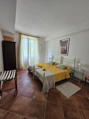 A bedroom with a bed, a chair, a bedside table, a lamp, and a window with curtains. - La Locanda del Tempo: an authentic stay combining charm, relaxation, and the real Italy. (Crocemarroggia)