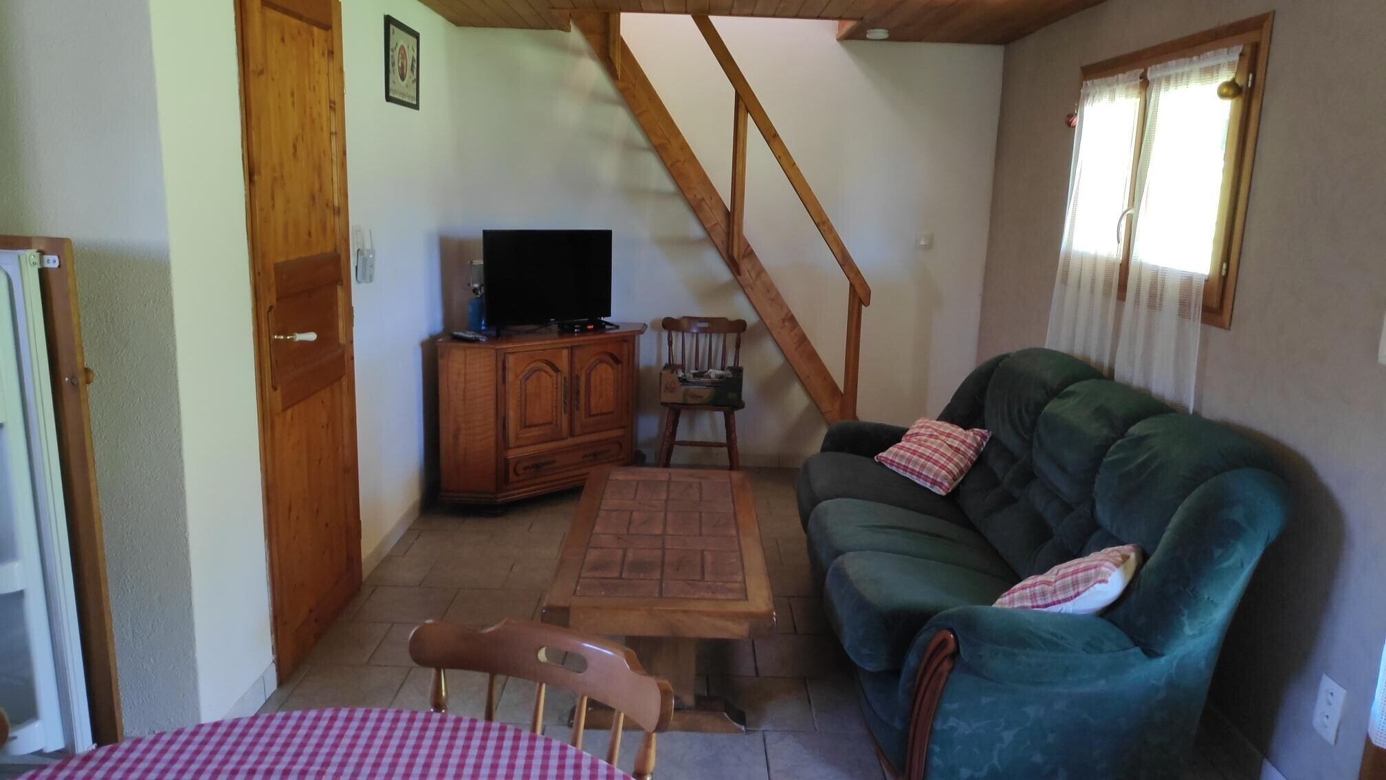 Een woonkamer met een bank, een televisie op een houten kast, een houten stoel en een tafel met een geruit tafelkleed.