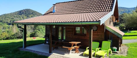 A wooden cabin with a tiled roof, a covered patio, and outdoor seating.