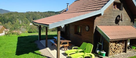 Een houten chalet met een overdekt terras, buitenmeubels en uitzicht op het omliggende landschap.
