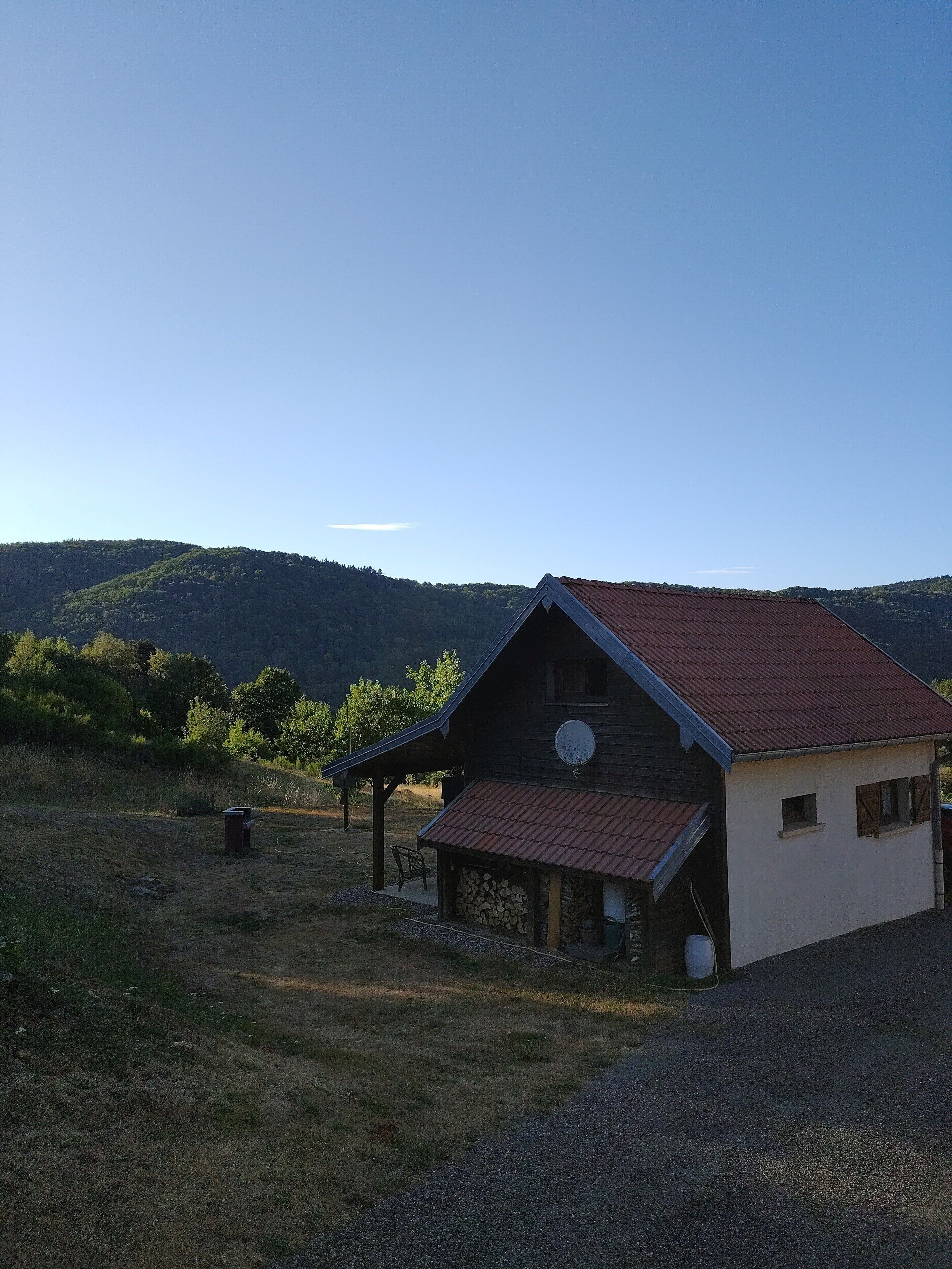 Une maison rustique en bois, dotée d’un toit en pente, d’une antenne parabolique et d’un porche abrité.