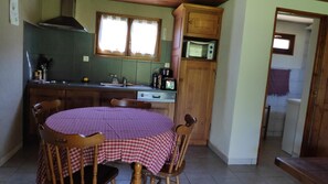 A kitchen with a dining table, chairs, a microwave, and a window with lace curtains. - Chalet "De montagne Milles Étangs": mountain view, private terraces and garden (Haut-du-Them-Château-Lambert)