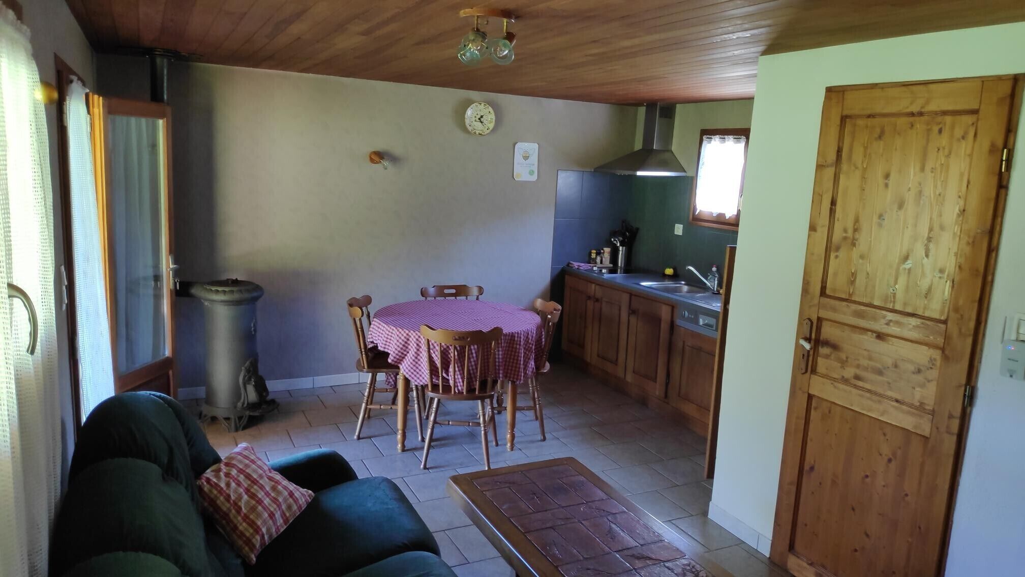 A cozy living room with a sofa, a dining table with chairs, a kitchen area with wooden cabinets, and a trash bin.
