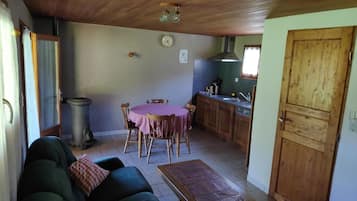 A cozy living room with a sofa, a dining table with chairs, a kitchen area with wooden cabinets, and a trash bin.
