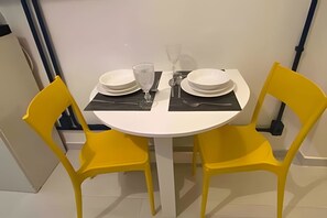 Ein Esstisch mit vier weißen Tellern, zwei Gläsern und Besteck, an beiden Seiten zwei gelbe Stühle.