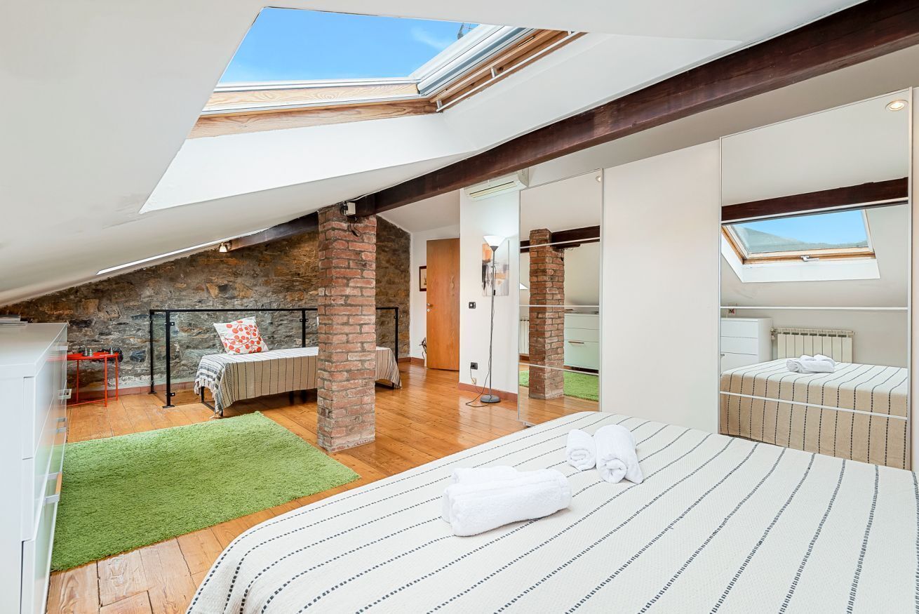 Ein geräumiges Schlafzimmer im Loftsstil mit Dachfenster, einem grünen Teppich, einem Bett mit gestreifter Bettwäsche und einer Ziegelwand.