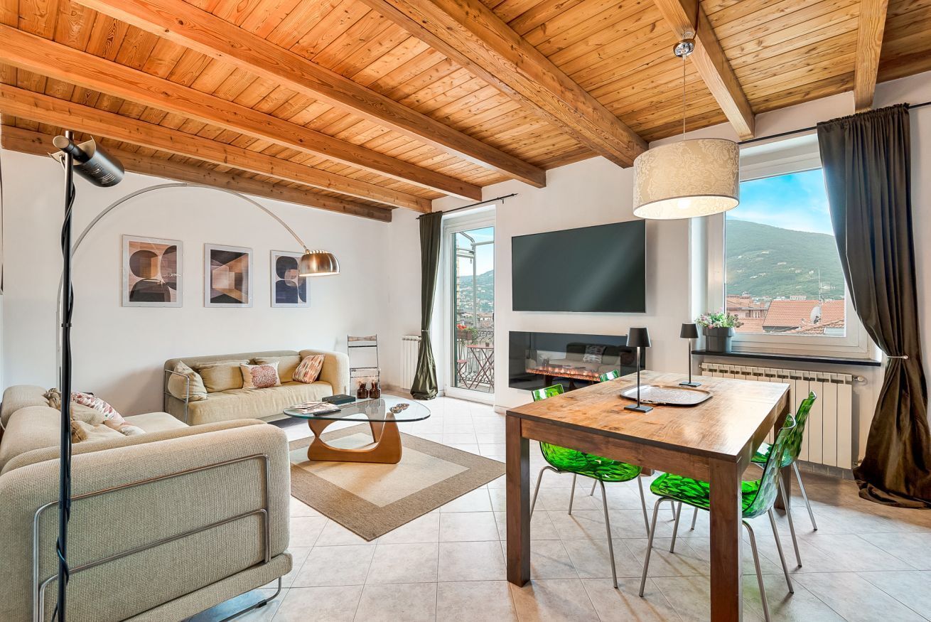 A modern living room with a wooden ceiling, a flat-screen TV, a fireplace, and a dining area with green chairs.