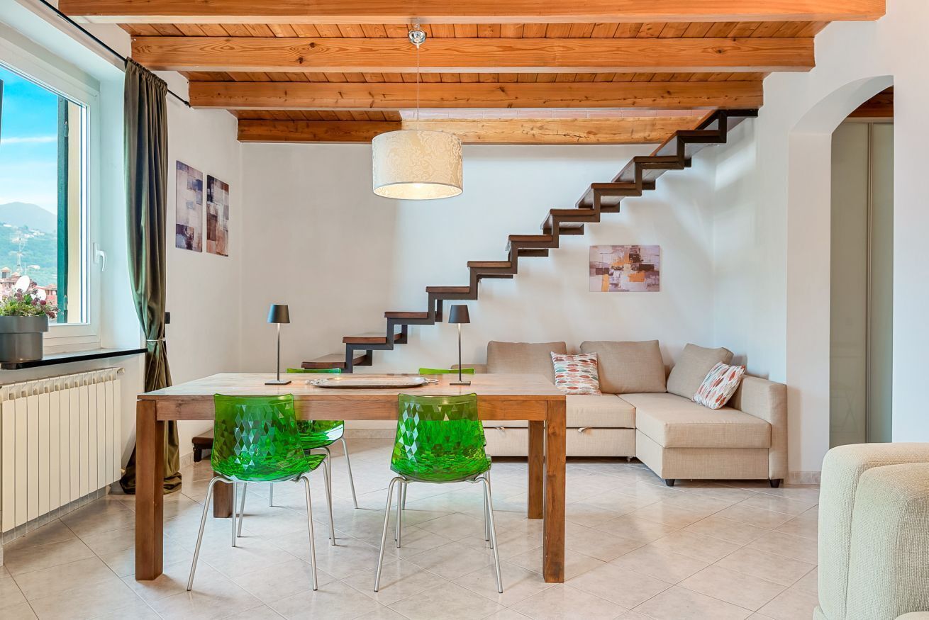 Ein modernes Interieur mit einer Holztreppe, einer Essecke mit grünen Stühlen und einem Sofa.