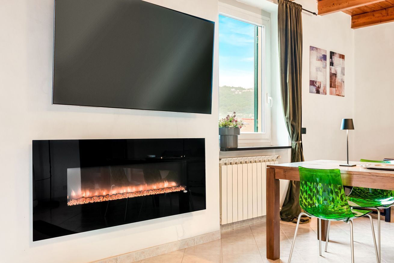 Ein modernes Wohnzimmer mit Kamin, Flachbildfernseher, Esstisch mit Stühlen und einem fenster mit Vorhängen.