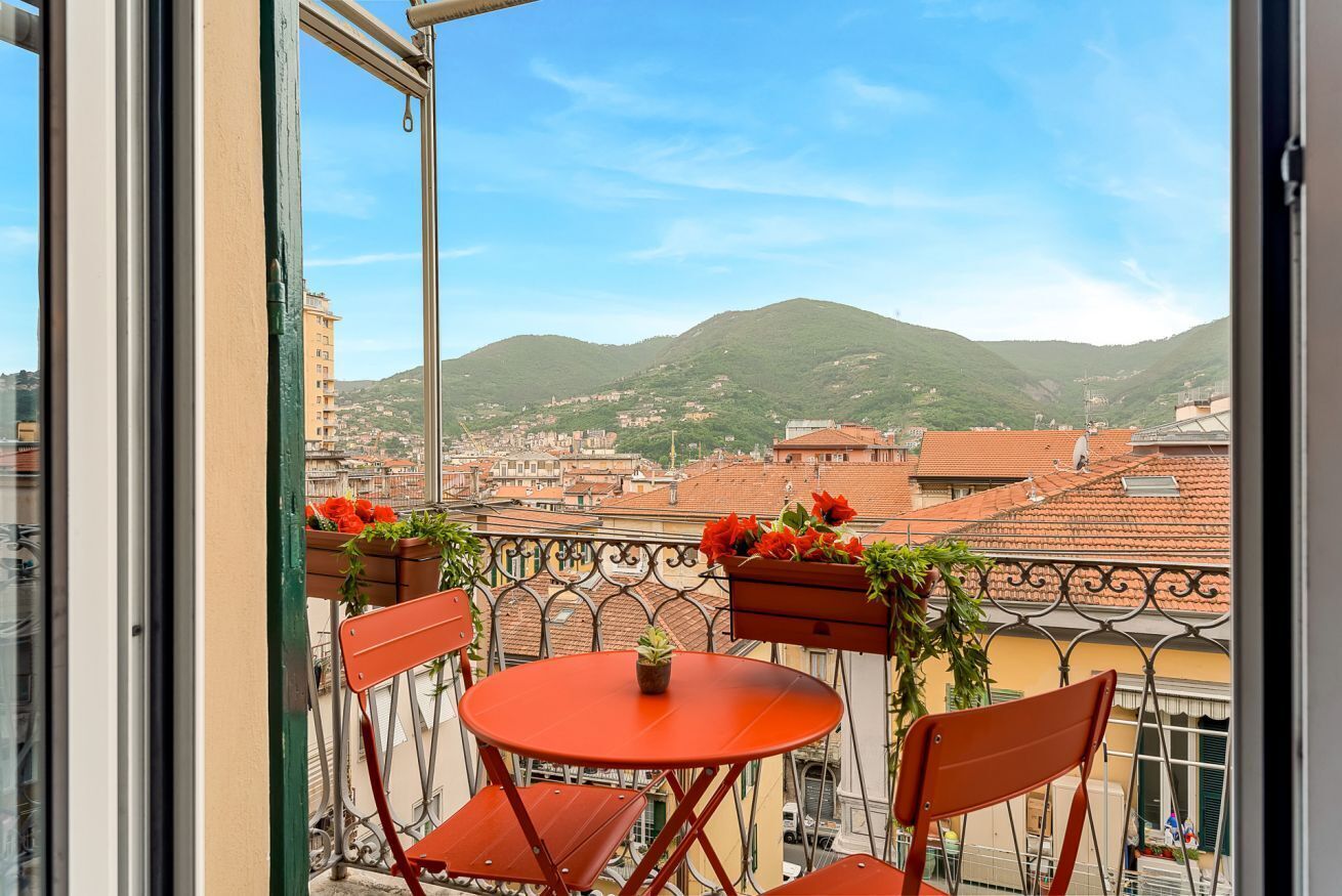 Un balcon avec une table et des chaises, donnant sur un paysage urbain avec des bâtiments et une colline.