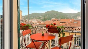Een balkon met een tafel en stoelen, met uitzicht op een stadsgezicht met gebouwen en een heuvel.