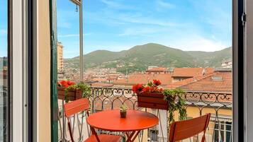 Un balcon avec une table et des chaises, donnant sur un paysage urbain avec des bâtiments et une colline.