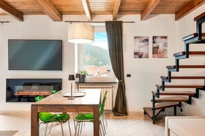 Ein modernes Wohnzimmer mit Kamin, einem Esstisch mit Stühlen, einem großen Flachbildfernseher und einer Treppe.