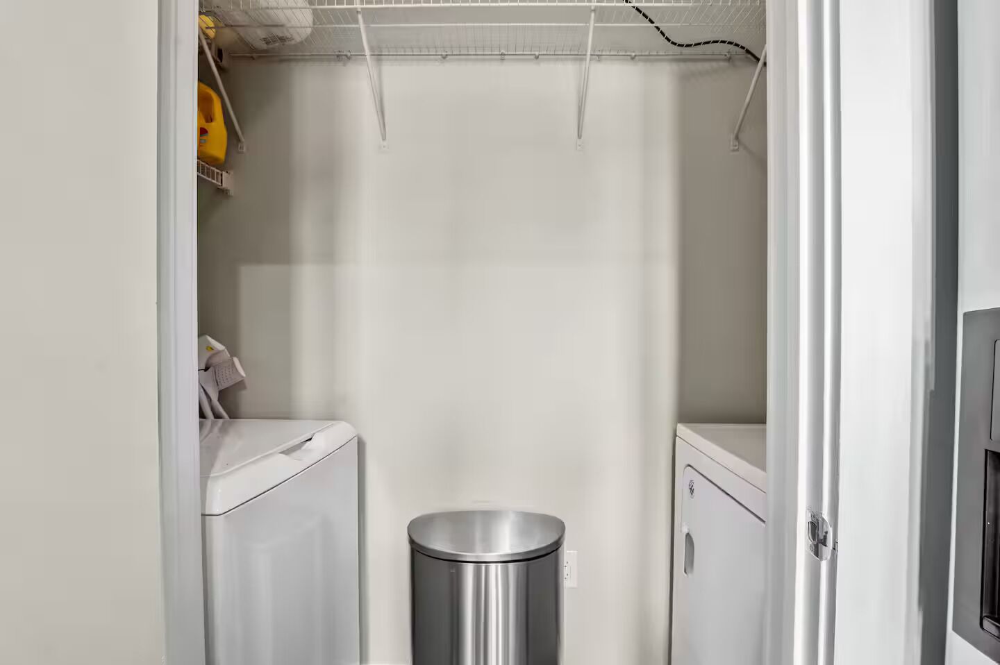 A laundry room with a washing machine, a dryer, and a trash can.