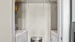 Een wasserette met een wasmachine, een droger en een prullenbak.