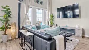Een moderne woonkamer met een zwarte leren bank, een flatscreen televisie aan de wand en een groot raam met uitzicht op de stad.