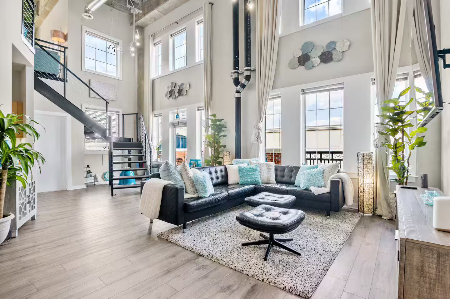 A spacious living area with a black leather sectional sofa, a staircase, and large windows.