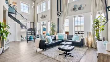 A spacious living area with a black leather sectional sofa, a staircase, and large windows.