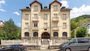 A multi-story building with a stone facade, multiple balconies, and a central entrance with steps. - Cocon d'Ax - Station de ski accessible à pied (Ax-les-Thermes)