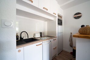 A compact kitchen with white cabinets, a black sink, a toaster, a kettle, and a microwave. - Cocon d'Ax - Station de ski accessible à pied (Ax-les-Thermes)