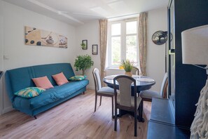 Ein Wohnzimmer mit einem blauen Sofa, einem Esstisch mit Stühlen, einer Topfpflanze und einem Wandbild.