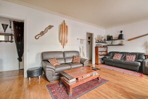 A living room with a brown leather sofa, a wooden coffee table, and a bookshelf filled with books and decorative items. - Appartement Parisien Haussmannien Ethnique (Paris)
