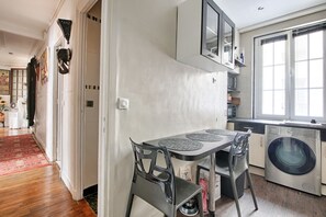 A compact kitchen with a washing machine, a dining table with chairs, and a window providing natural light. - Appartement Parisien Haussmannien Ethnique (Paris)
