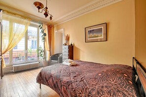Ein Hotelzimmer mit Bett, einem Sessel, einem Heizkörper, einem Fenster mit Vorhängen und einem Bild an der Wand.