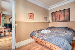 A bedroom with a wooden bed, a tapestry on the wall, and a small table with a plant. - Appartement Parisien Haussmannien Ethnique (Paris)
