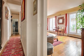 A hallway leading to a dining area with a red patterned rug, a dining table with chairs, and a large window with curtains. - Appartement Parisien Haussmannien Ethnique (Paris)