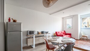 A compact kitchen with a refrigerator, microwave, and toaster, a dining area with a round table and chairs, and a red sofa. - Le Maryland - Climatisé à 100 m de la plage (Leucate)