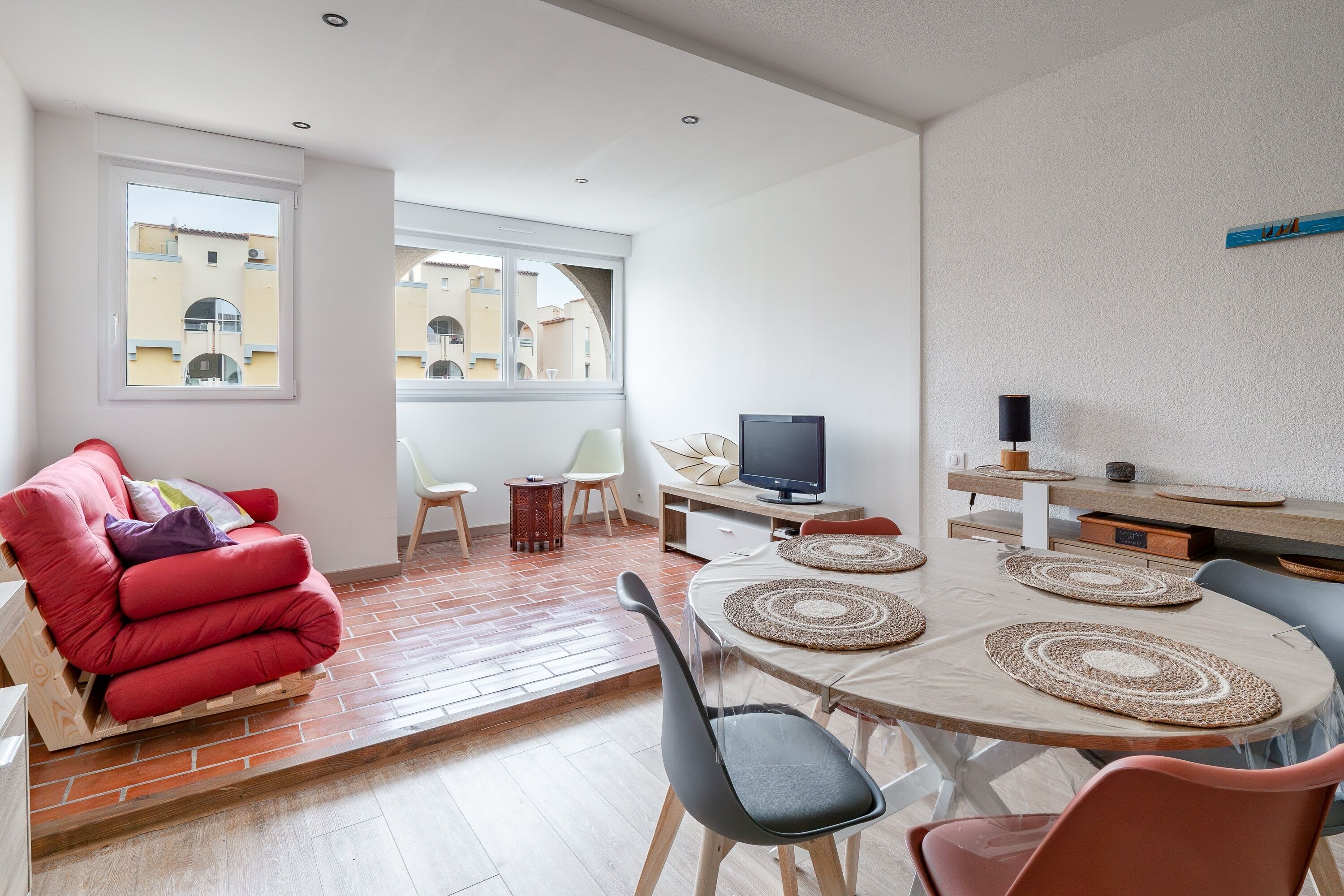 A modern living room with a red sofa, a TV, and a dining area with a table and chairs.