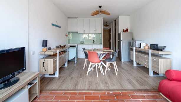 A compact living space with a kitchen, dining area, and a TV on a wooden stand. - Le Maryland - Climatisé à 100 m de la plage (Leucate)