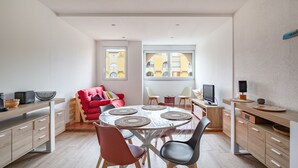 A modern kitchen with a dining area, featuring a round table with placemats, wooden cabinets, and a red chair. - Le Maryland - Climatisé à 100 m de la plage (Leucate)