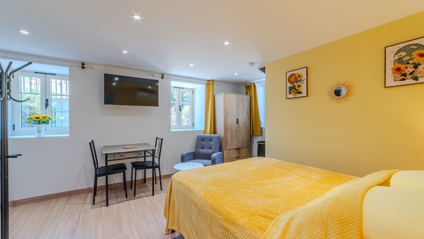 Una habitación de hotel con cama, un escritorio con silla, televisor y ventana con cortinas.