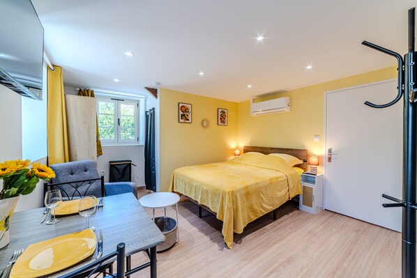 Een knus slaapkamer met een bed, nachtkastje en een eettafel met stoelen.